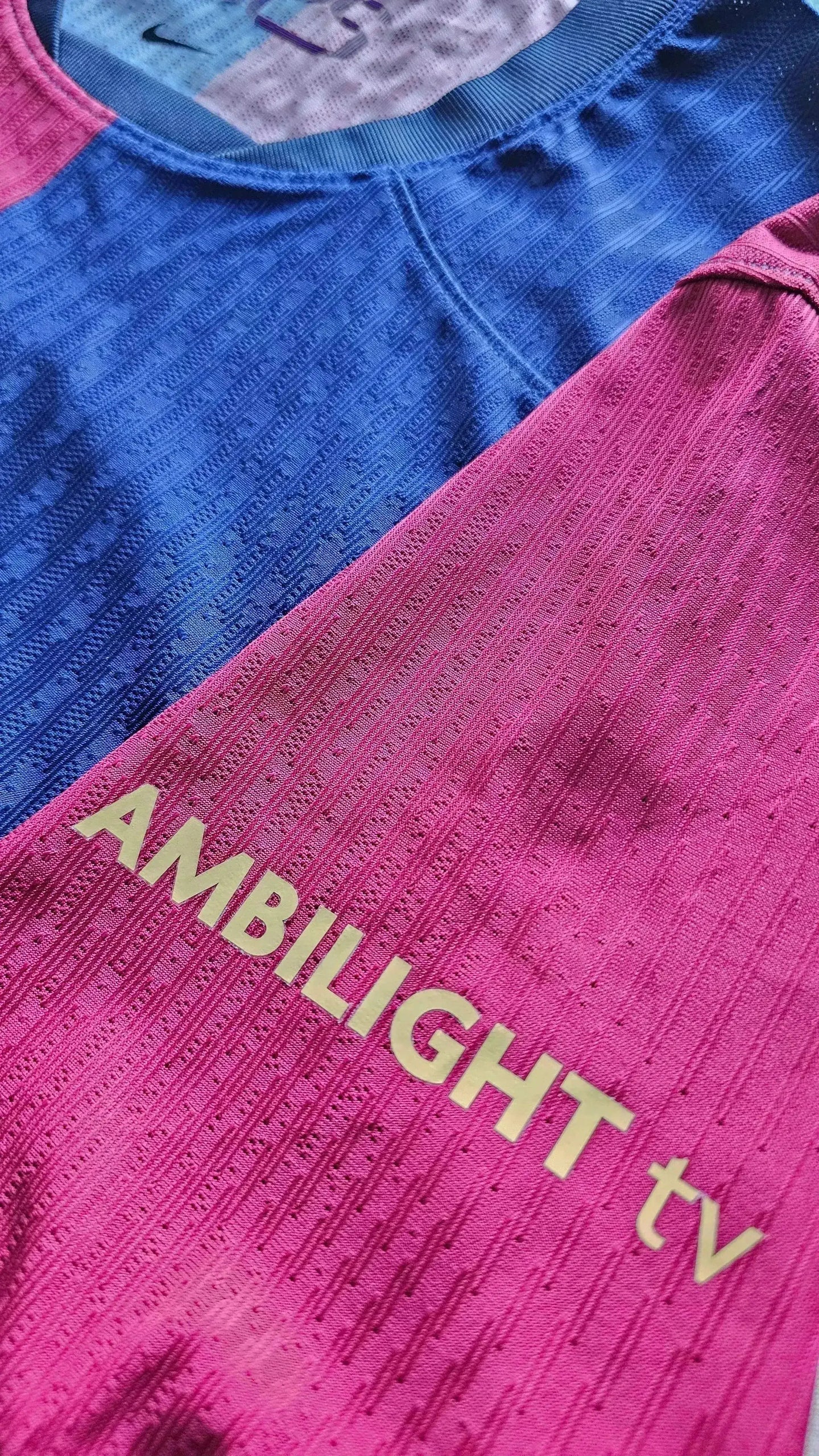 Close-up of the collar and shoulder of a football shirt featuring AMBILIGHT tv text in gold.