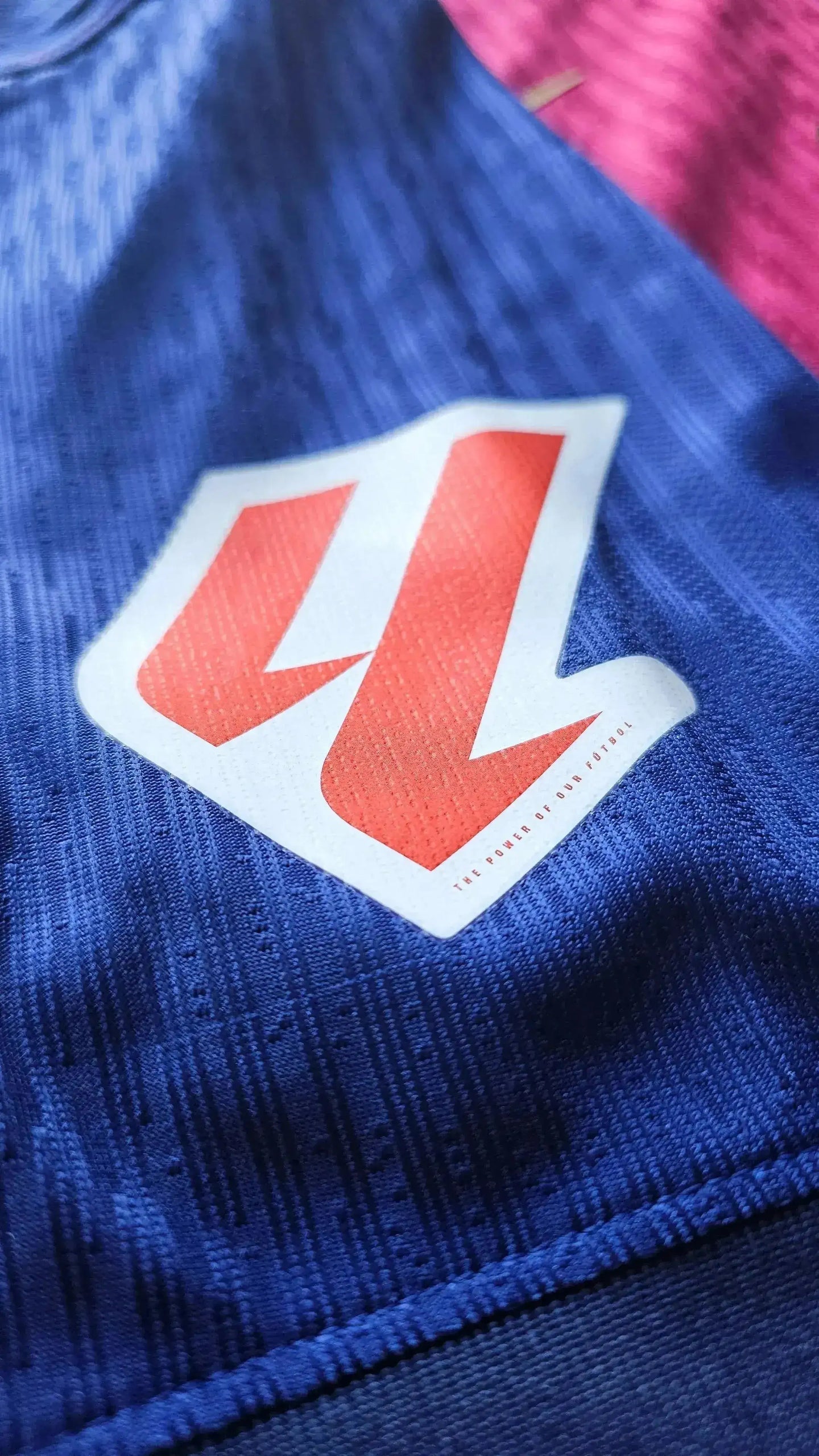 Close-up of logo featuring a red and white design with text 'THE POWER OF OUR FUTBOL'.