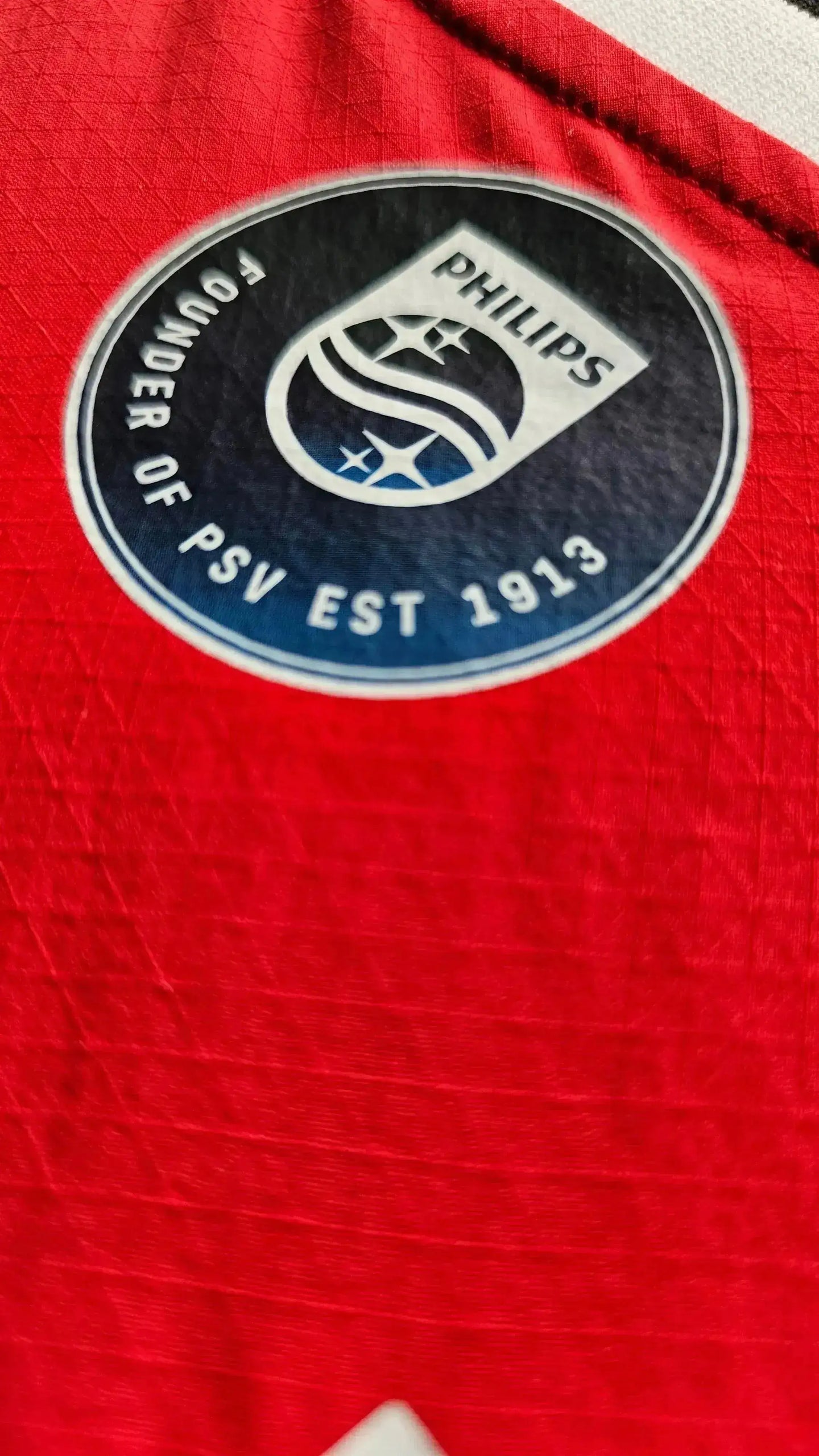 Crest detail of PSV Eindhoven shirt featuring 'PHILIPS' and 'FOUNDER OF PSV EST 1913' text.