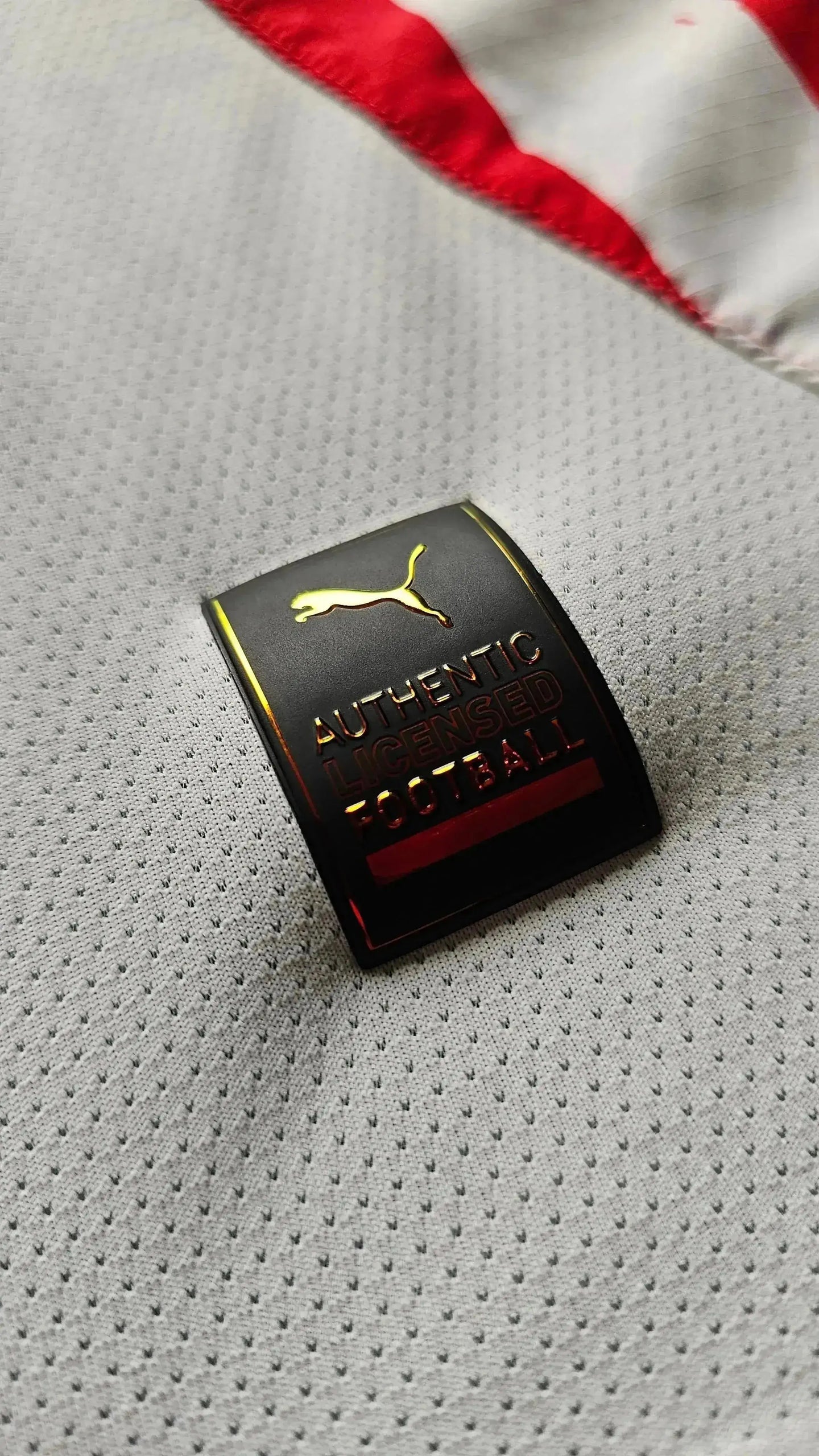 Close-up of black tag reading 'AUTHENTIC LICENSED FOOTBALL' with a gold Puma logo.