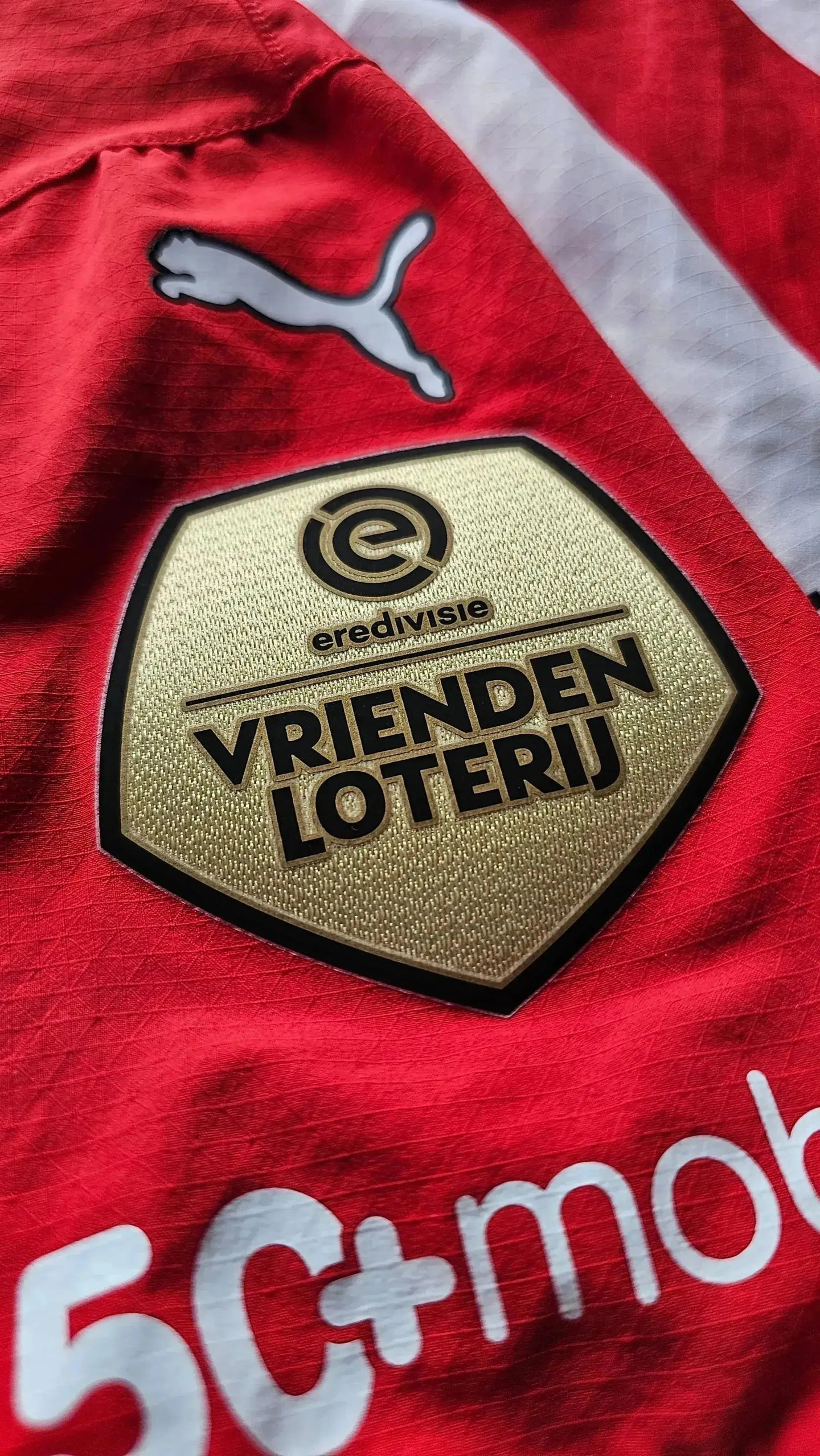 Detail view of PSV Eindhoven logo and Vrienden Loterij badge on a red football shirt.