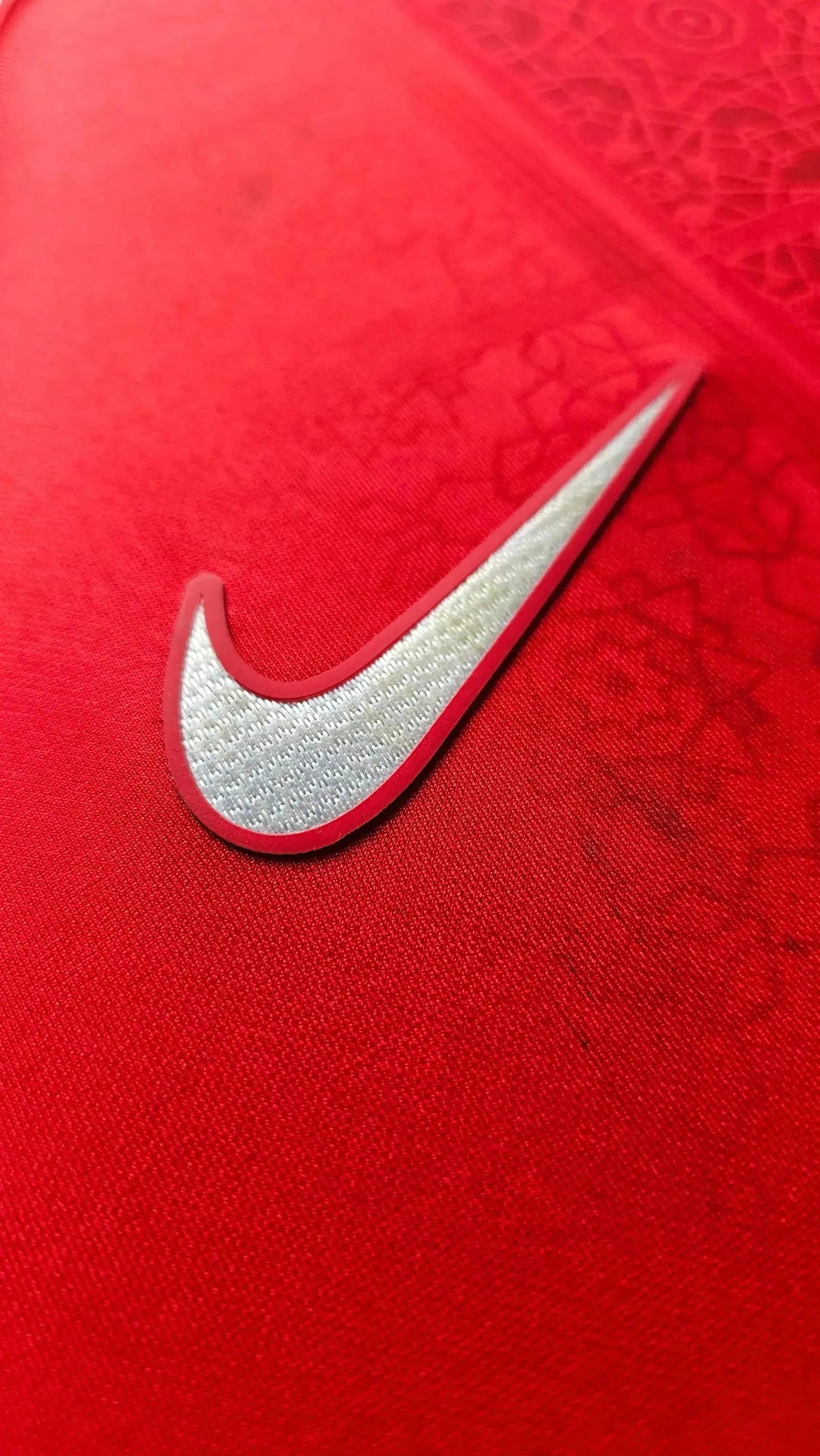 Close-up detail of the Nike logo on a red football shirt.