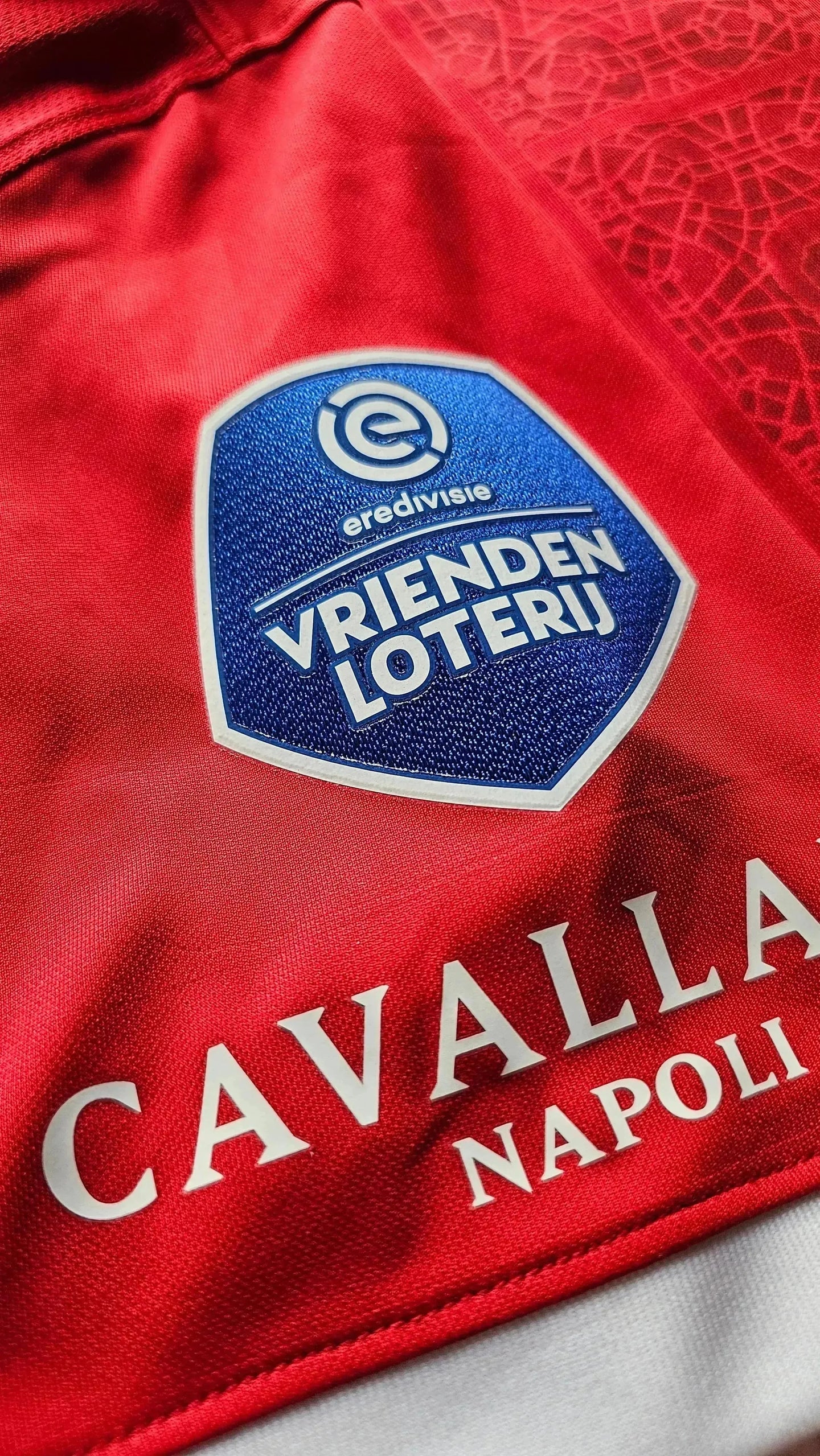 Crest detail featuring Vrienden Loterij and Cavalla Napoli on a red football shirt.