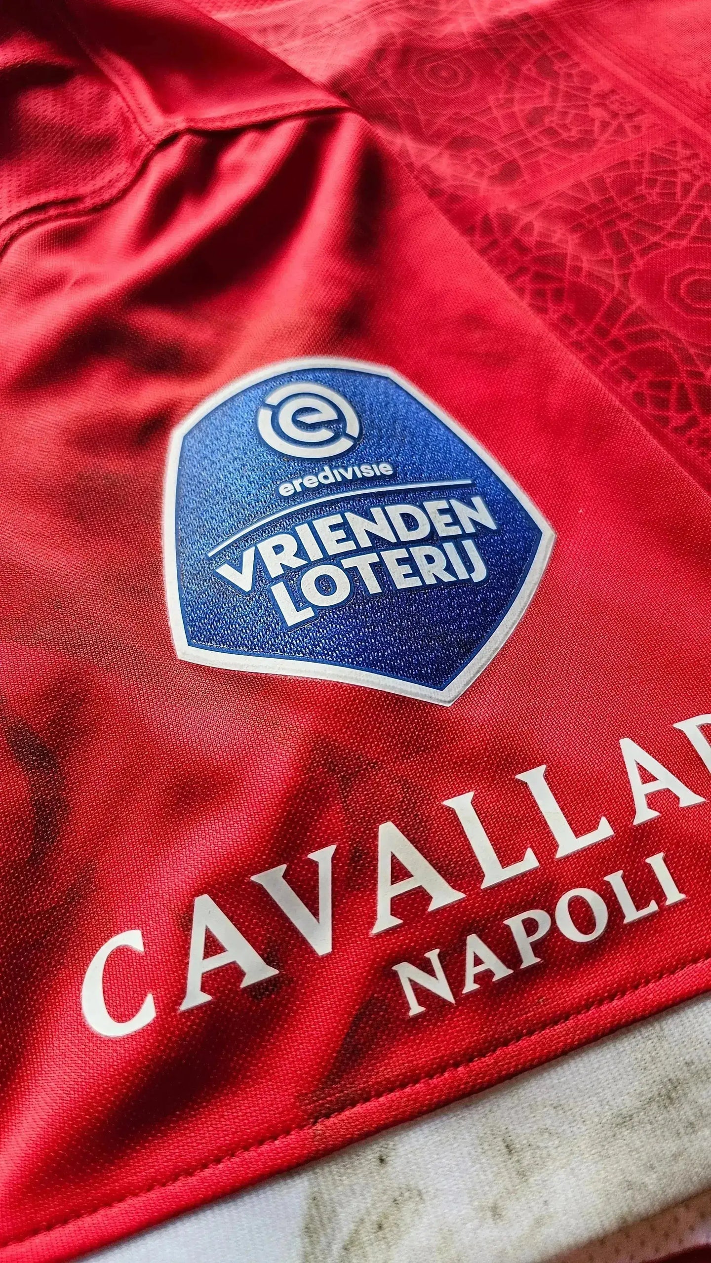 Close-up of the VRIENDEN LOTERIJ logo on a red football shirt with CAVALLAD NAPOLI text.