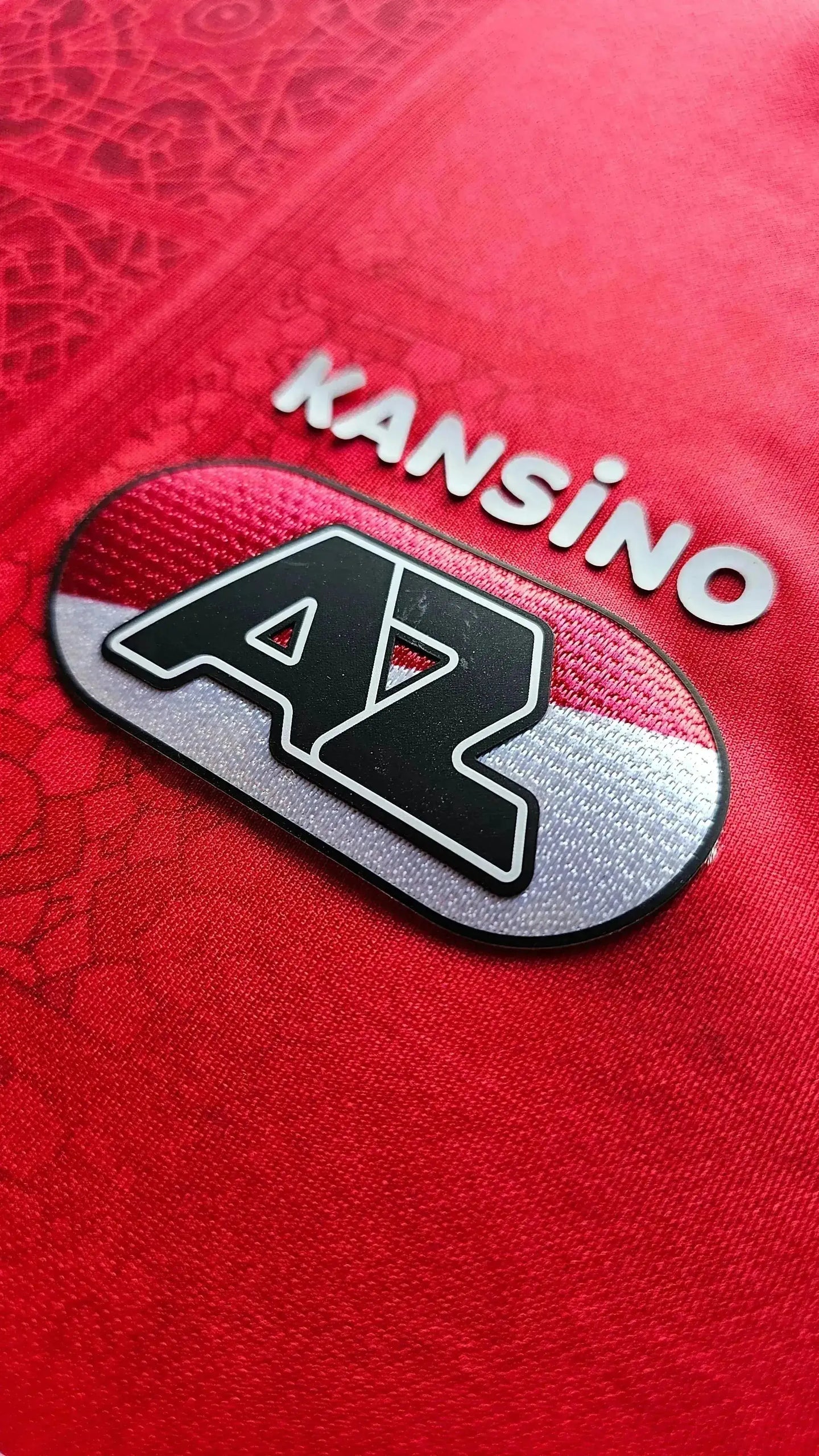Detail view of AZ Alkmaar crest with KANSINO text on a red football shirt.