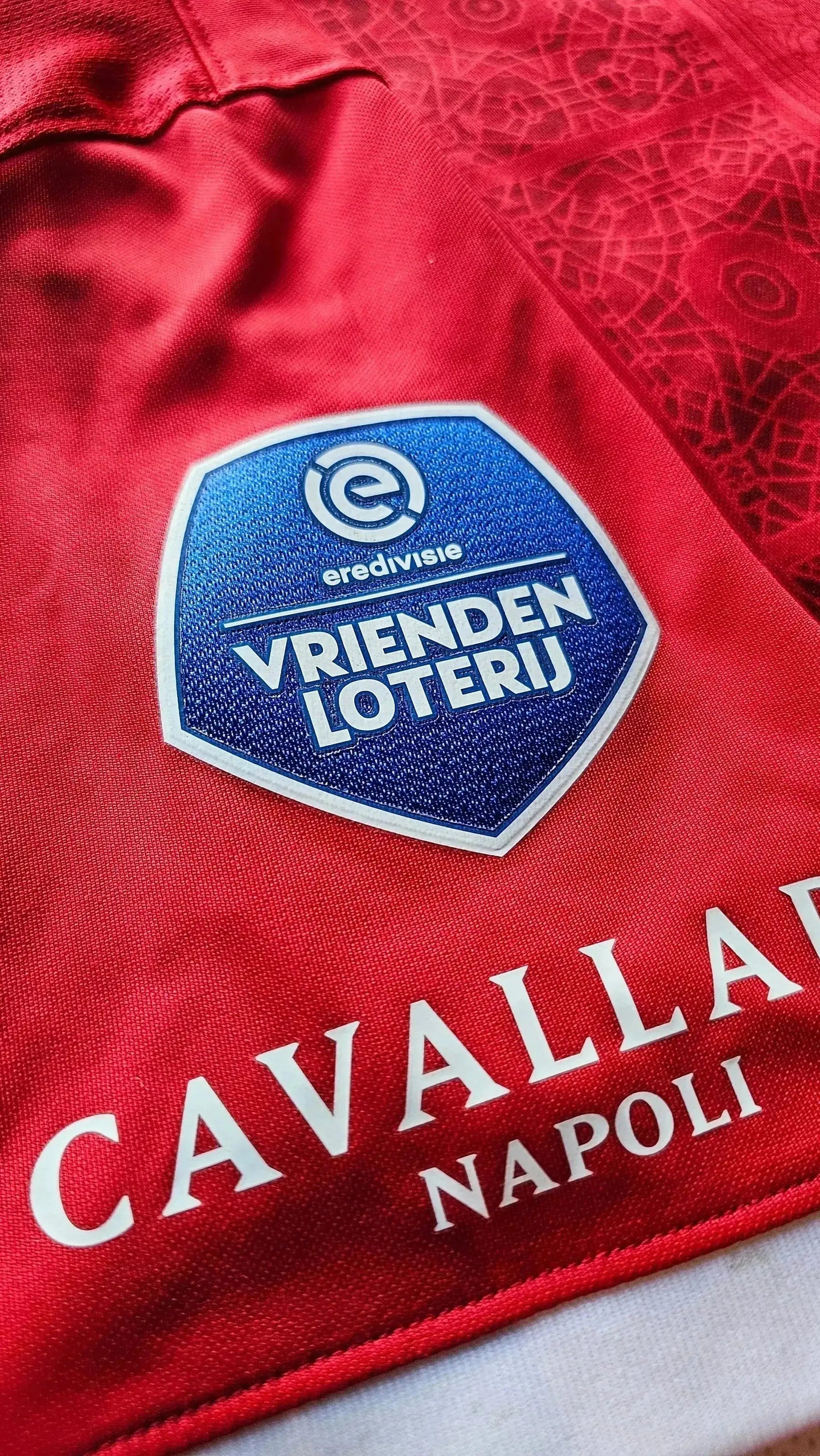 Close-up of crest detail showing VRIENDEN LOTERIJ and CAVALLARIA NAPOLI on a red shirt.