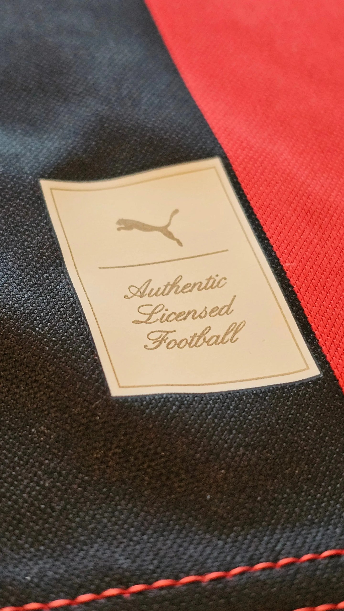 Puma tag showing 'Authentic Licensed Football' on black and red fabric.