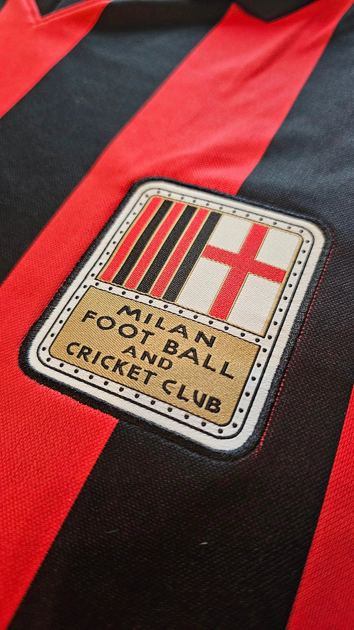 AC Milan crest with text 'MILAN FOOT BALL AND CRICKET CLUB' embroidered on black and red stripes.