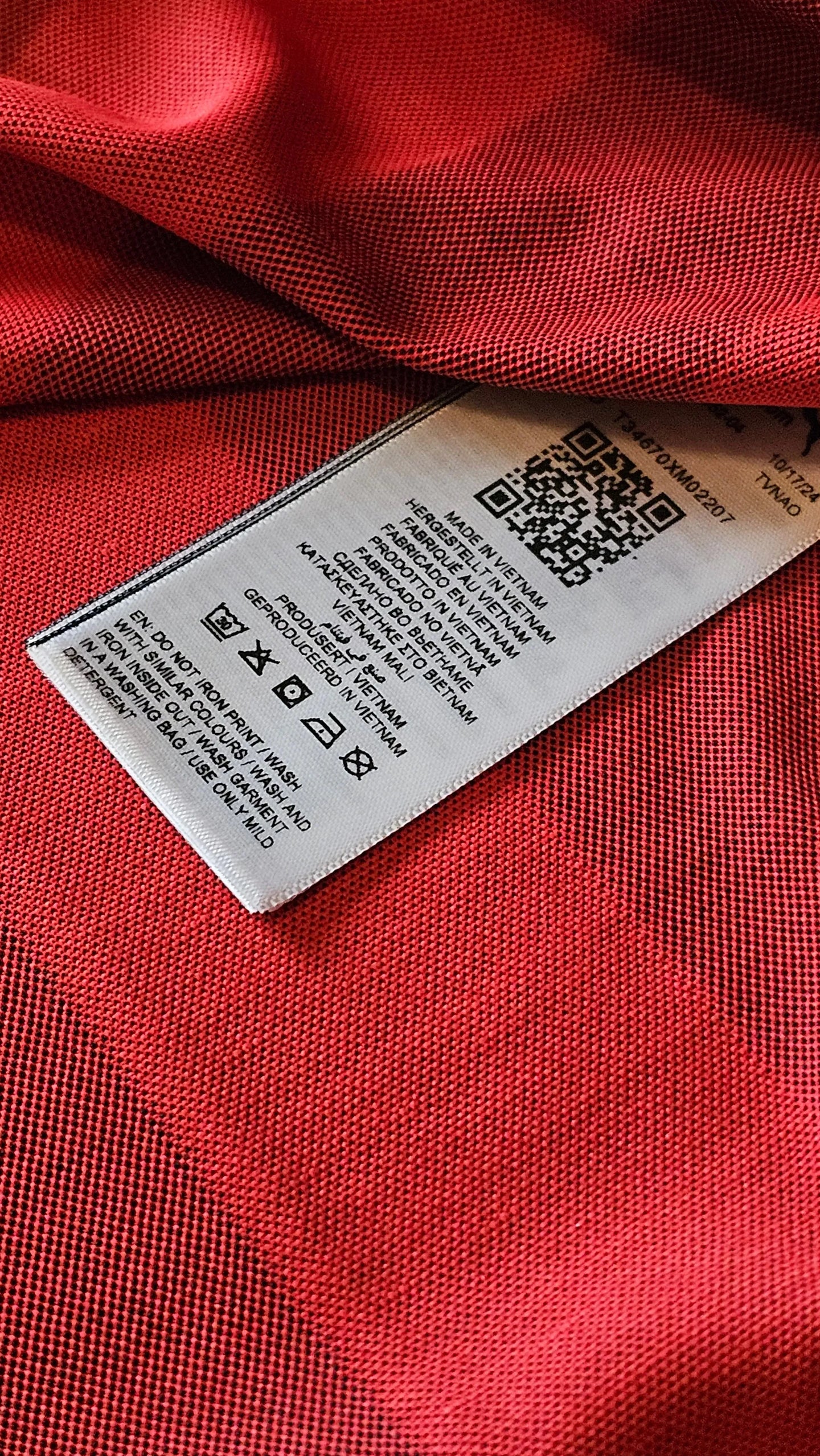 Care label showing care instructions and QR code on red fabric background.