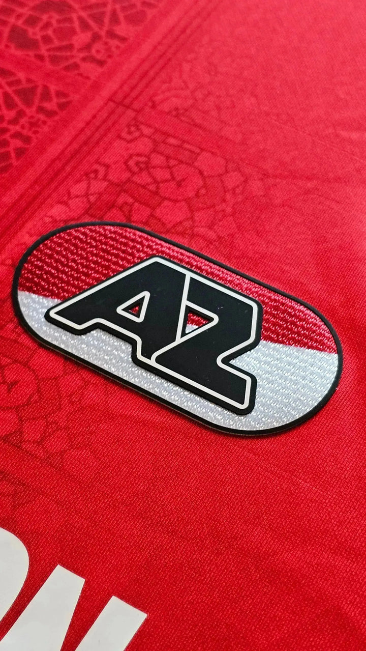 AZ Alkmaar crest detail on a red football shirt with white and black elements.