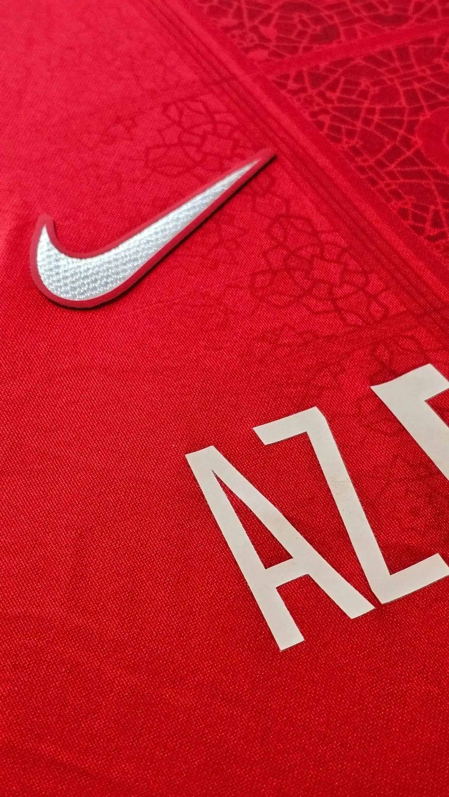 Close-up of AZ Alkmaar crest detail and Nike logo on red football shirt.