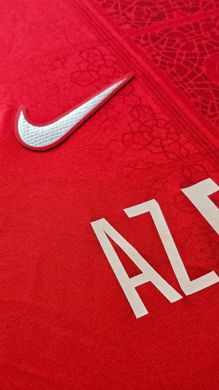Close-up of AZ Alkmaar crest detail and Nike logo on red football shirt.