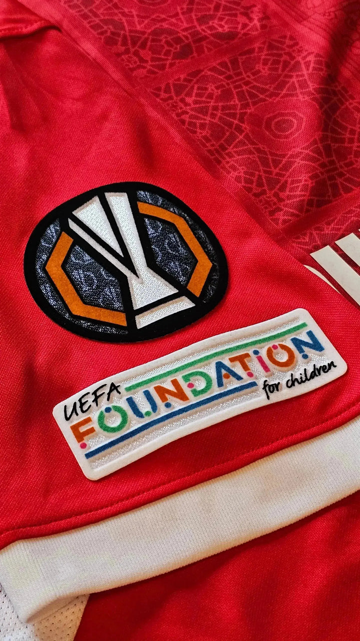 Detail showing UEFA Europa League badge and UEFA Foundation for Children logo on the red shirt.