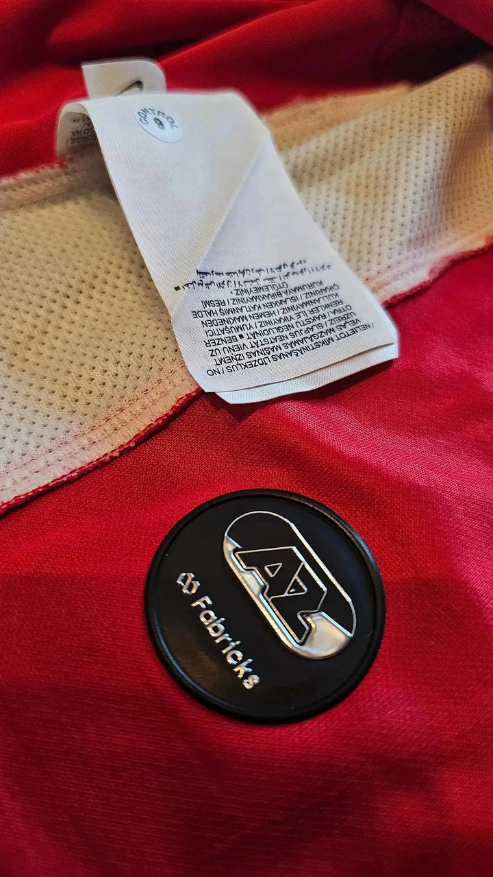 Crest detail featuring AZ Alkmaar emblem and 'Fabriticks' wordmark on red background.