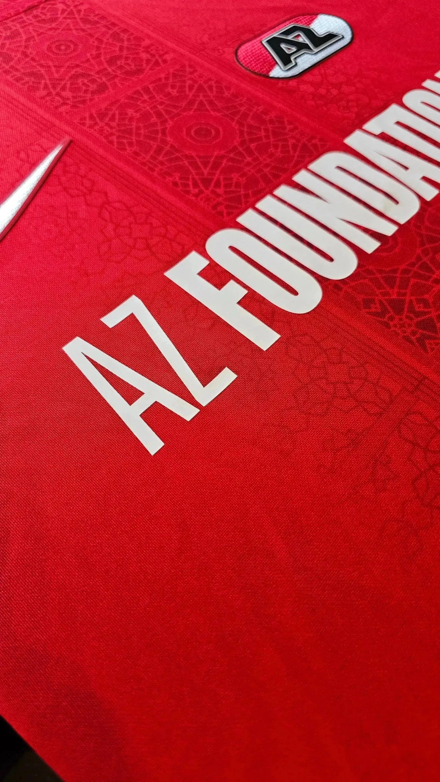 AZ Foundation logo printed in white on a red football shirt with intricate pattern detail.