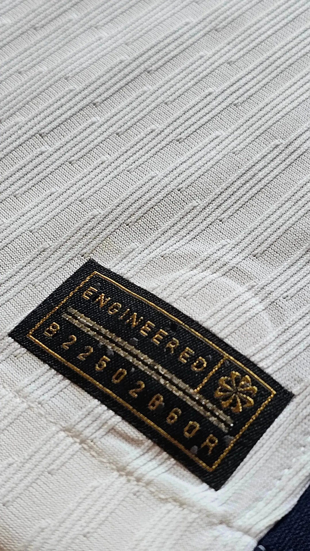 Detailed view of the white textile pattern with an embroidered label reading 'ENGINEERED 922502860R'.