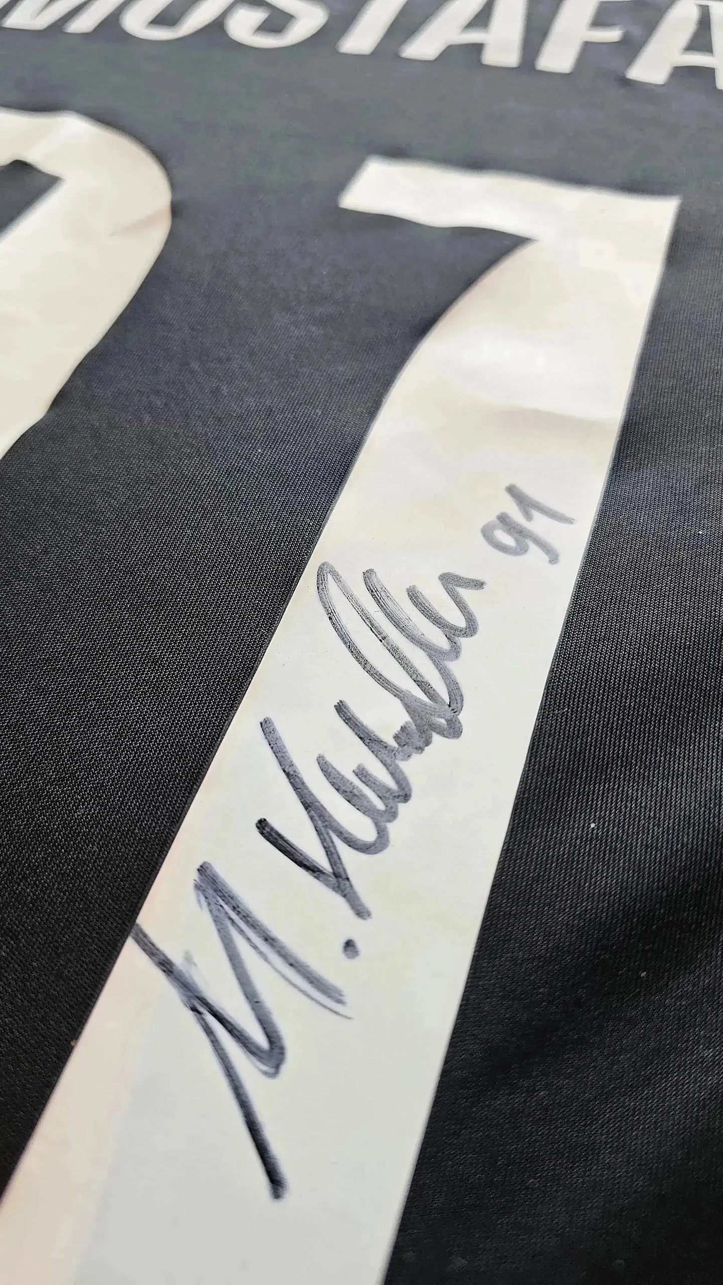 Signature detail showing M. Mustafa 91 on a black football shirt.