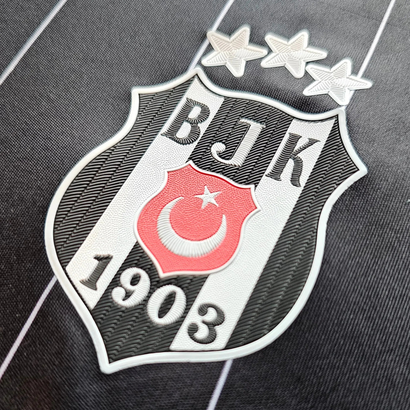 Beşiktaş JK crest on a black football shirt with thin white pinstripes, black and white shield with a red crescent and star and three white stars above, 1903 lettering.