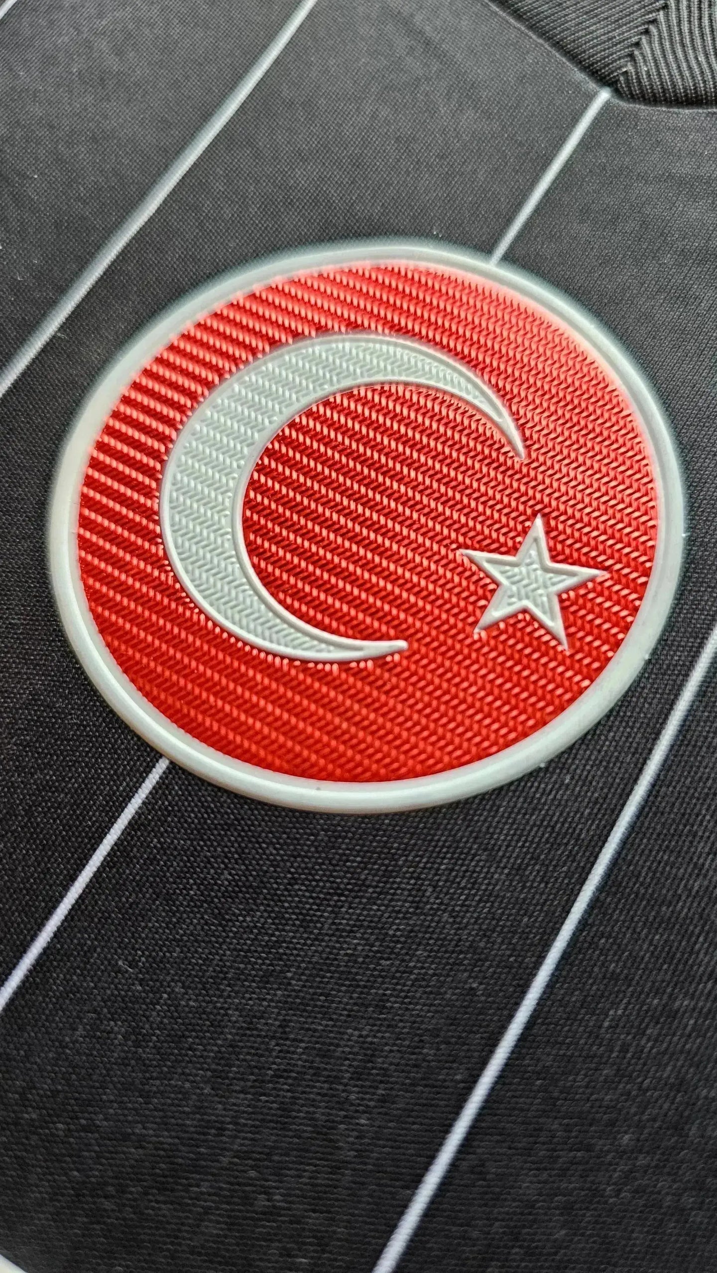 Crest detail showing the red crescent and star on a black football shirt.