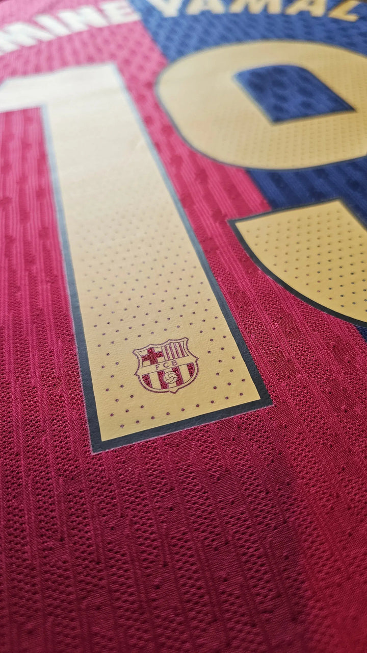 Close-up view showing the FCB crest and player name Yamal with No. 19 on a red and blue background.
