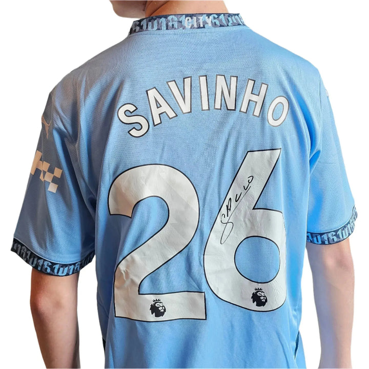 Back view showing Savinho, No. 26, and signature detail on a blue football shirt.