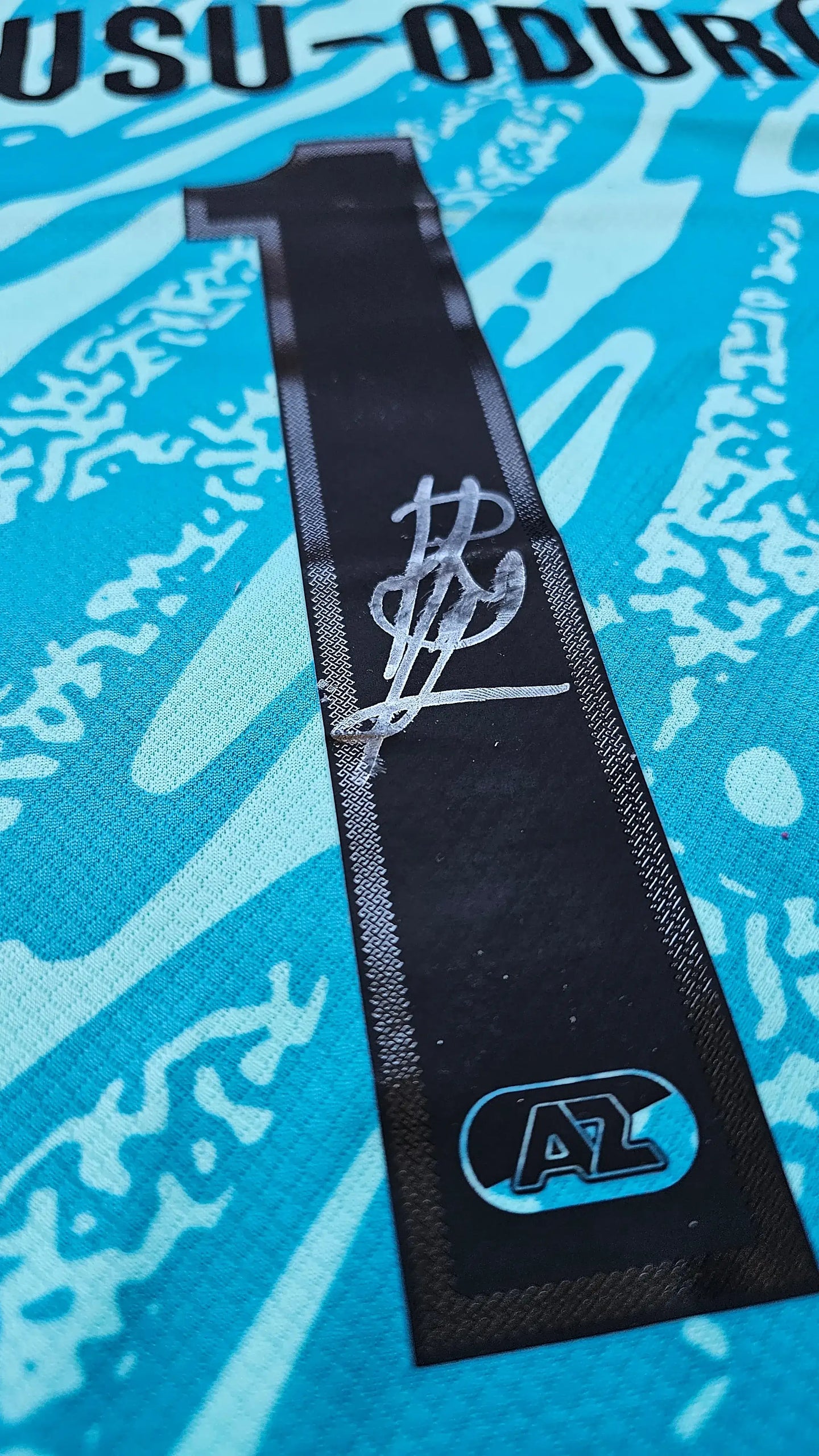 Close-up of Owusu-Oduro written in black, above No. 1 on blue football shirt with AZ logo.