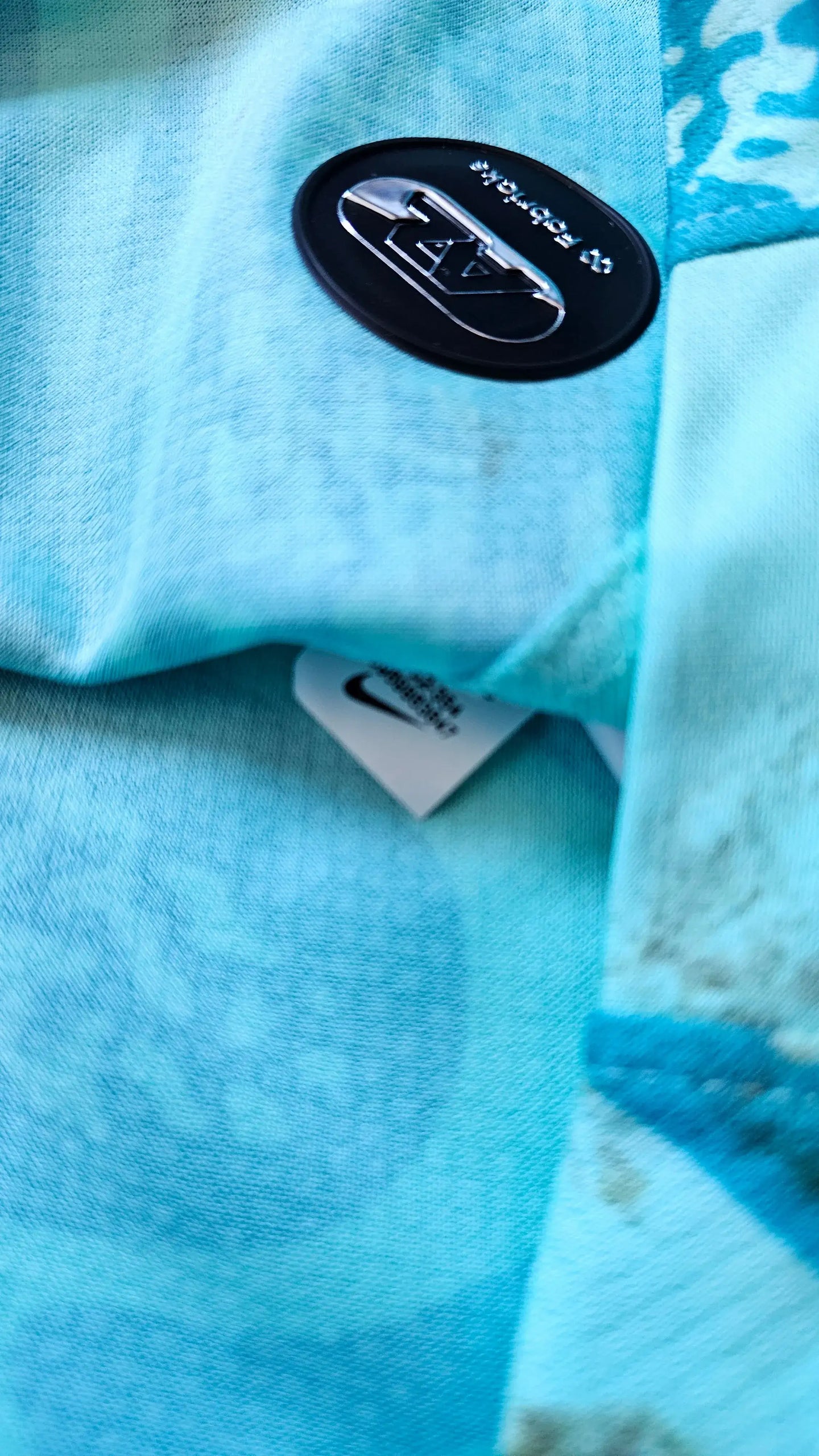 Close-up of AZ Alkmaar crest detail on blue shirt with Nike tags visible.