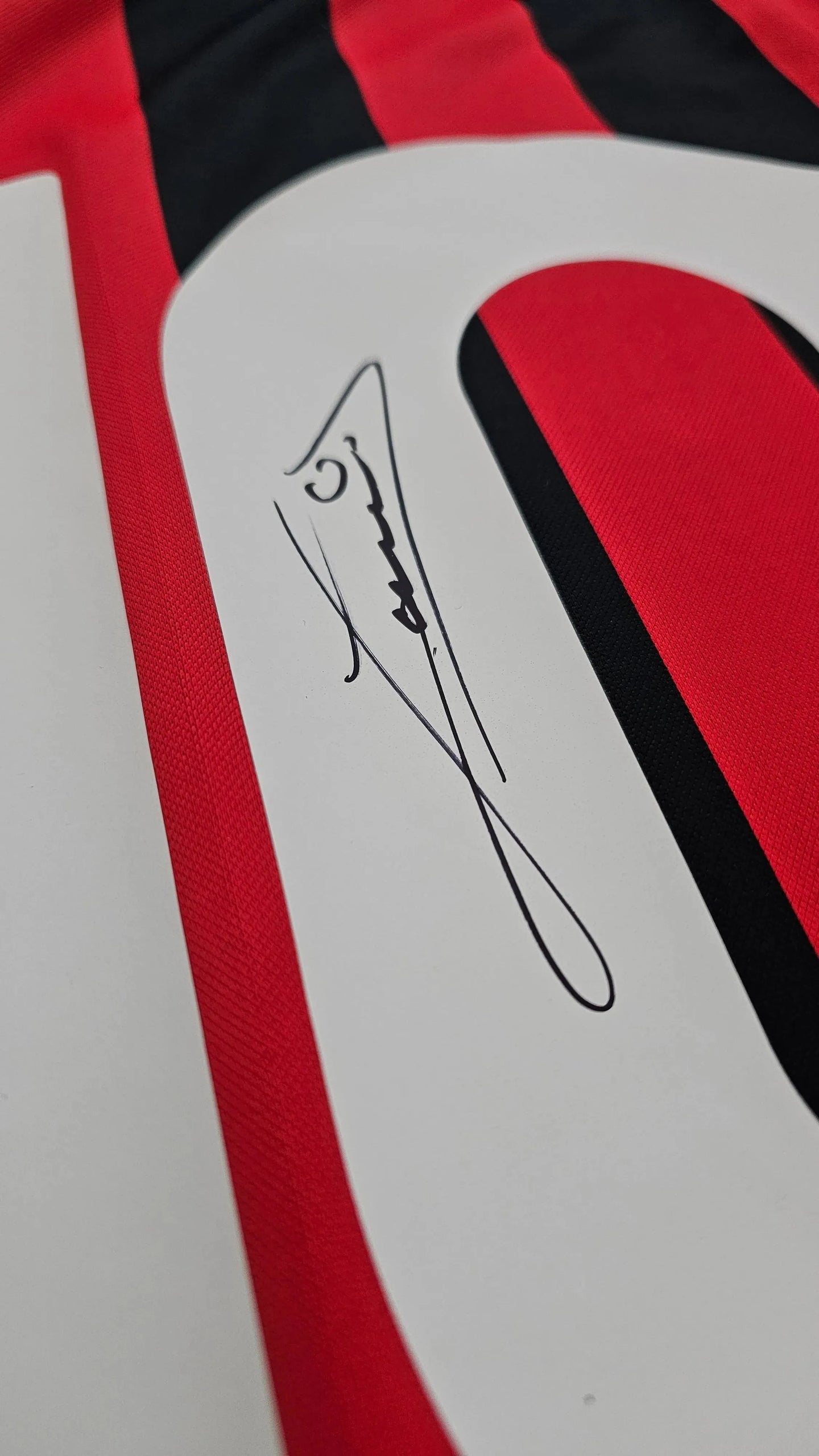 Close-up of the signature detail on the No. 10 AC Milan football shirt in red and black stripes.