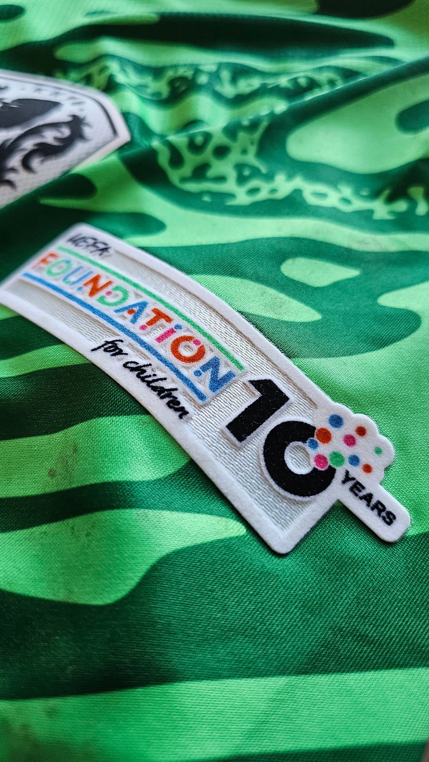 Detail showing foundation patch with text '10 YEARS' and 'FOUNDATION for children' on green fabric.