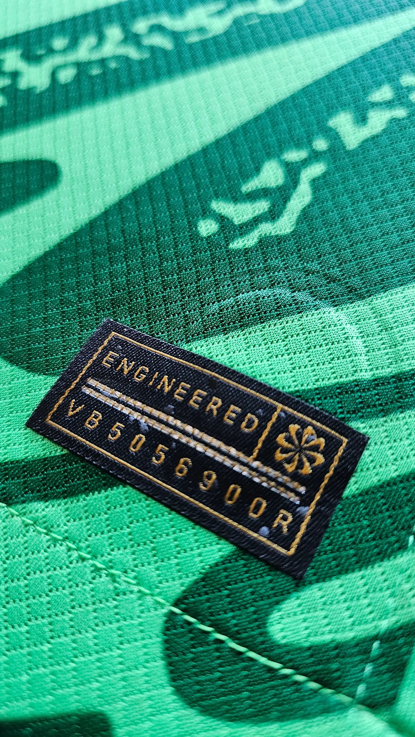 Close-up showing the 'ENGINEERED' label with code VB5056900R on a green football shirt.