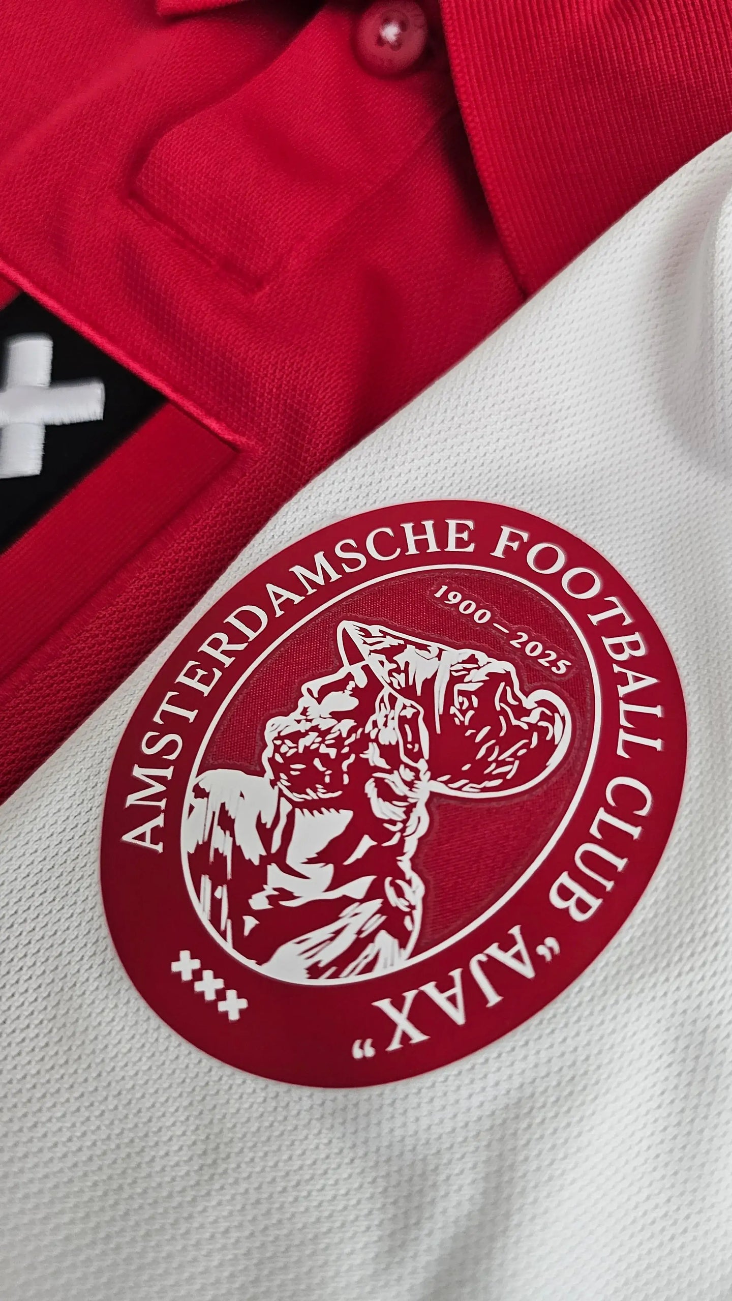 Close-up of AFC Ajax crest featuring 1900-2025 and player details in red and white.