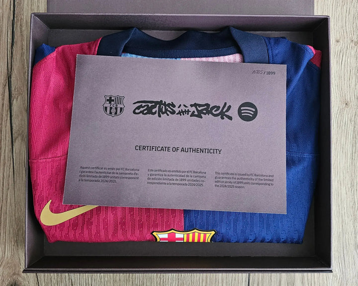 Packaged football shirt with a certificate of authenticity on a wooden surface.
