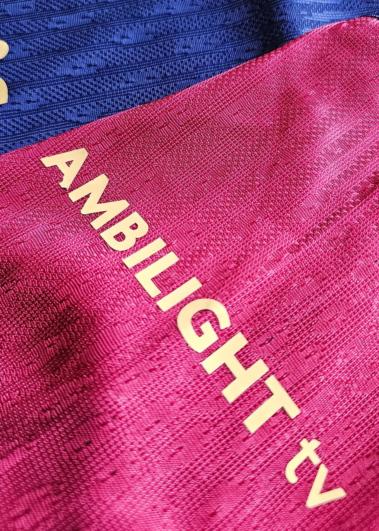 Crest and sponsor detail with 'AMBI-LIGHT tv' text on red and blue sections of soccer jersey.