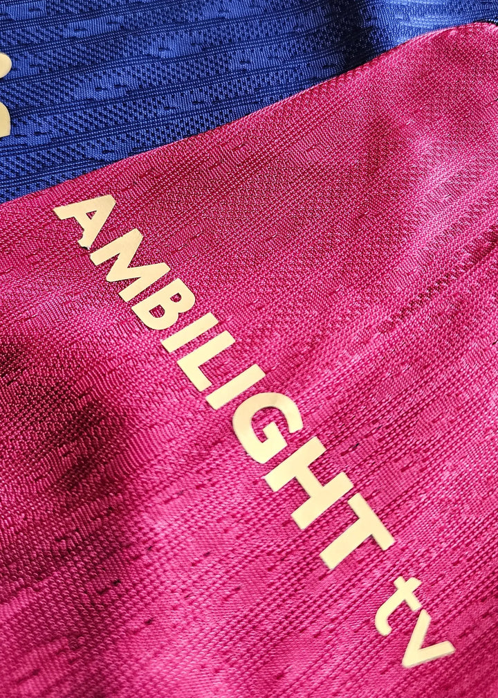Crest and sponsor detail with 'AMBI-LIGHT tv' text on red and blue sections of football shirt.
