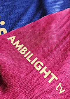 Detail showing the AMBILIGHT tv sponsor on a blue and red Barcelona football shirt.