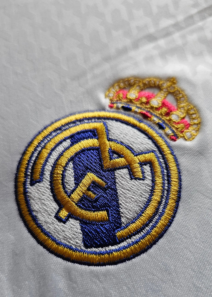 Embroidered Real Madrid CF crest with crown detail on a white football shirt.