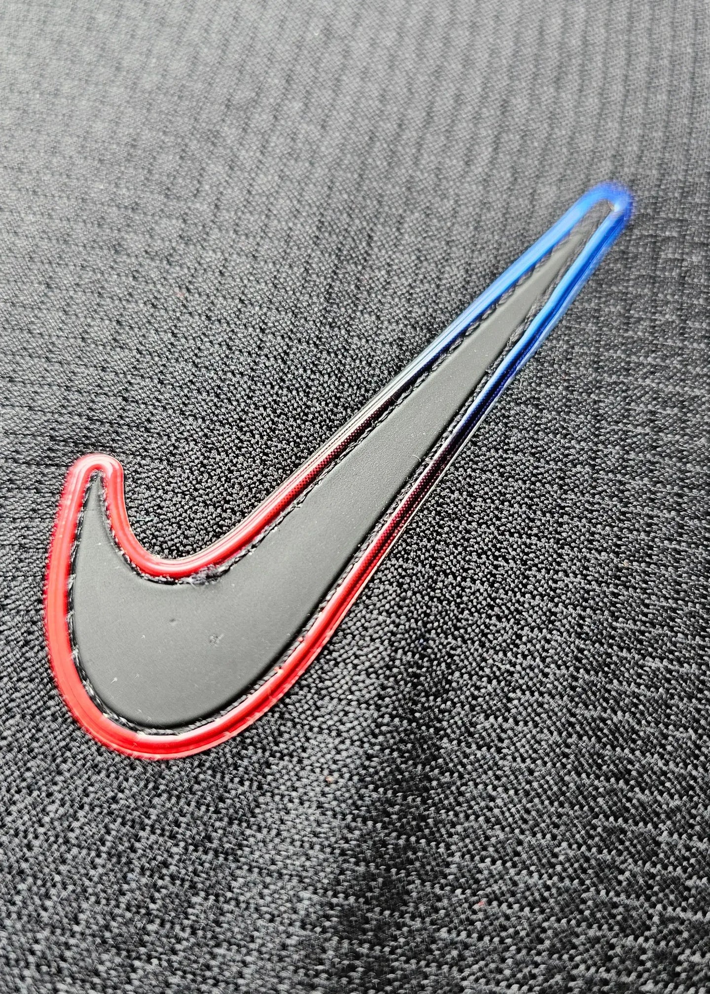 Detail of the Nike logo in red and blue on a black football shirt fabric.