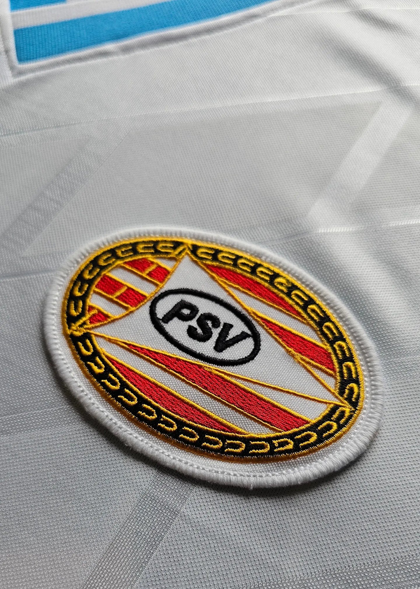 Crest detail showing the PSV badge featuring red and yellow stripes on a white background.