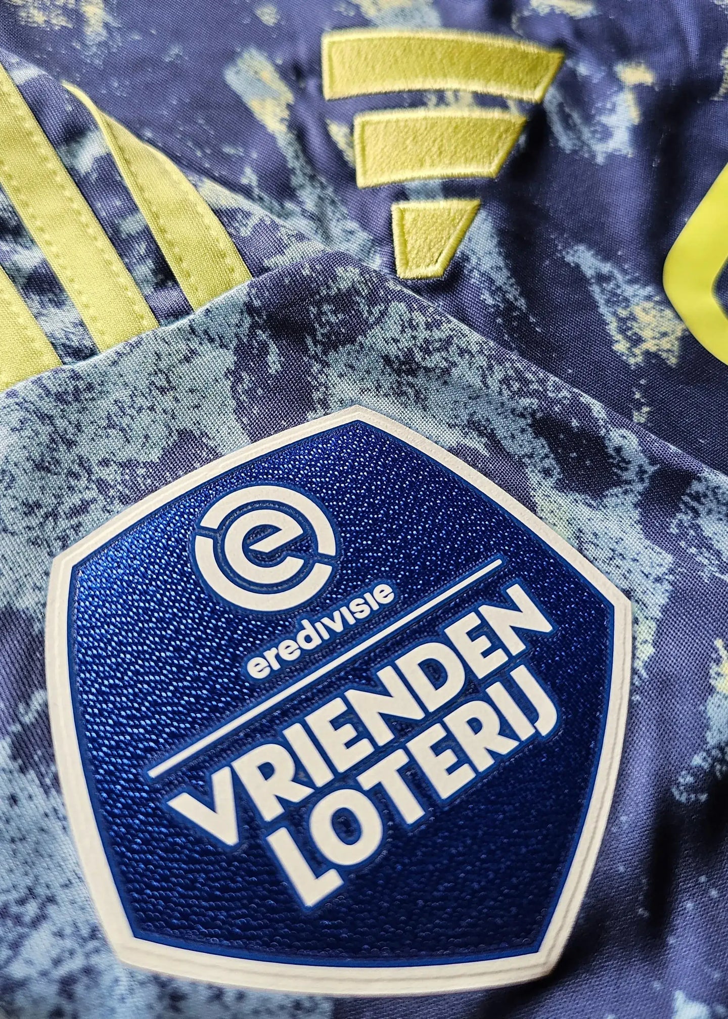 Close-up of the Eredivisie and Vrienden Loterij logos with yellow accents on a blue background.