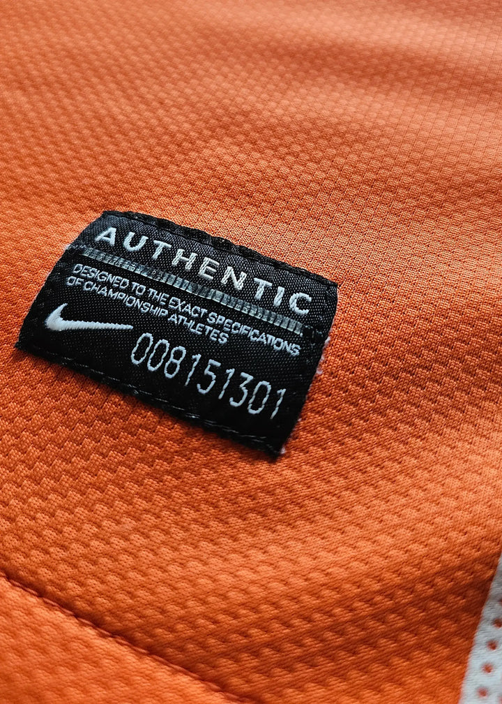 Close-up of the 'AUTHENTIC' tag and care instructions on an orange football shirt.