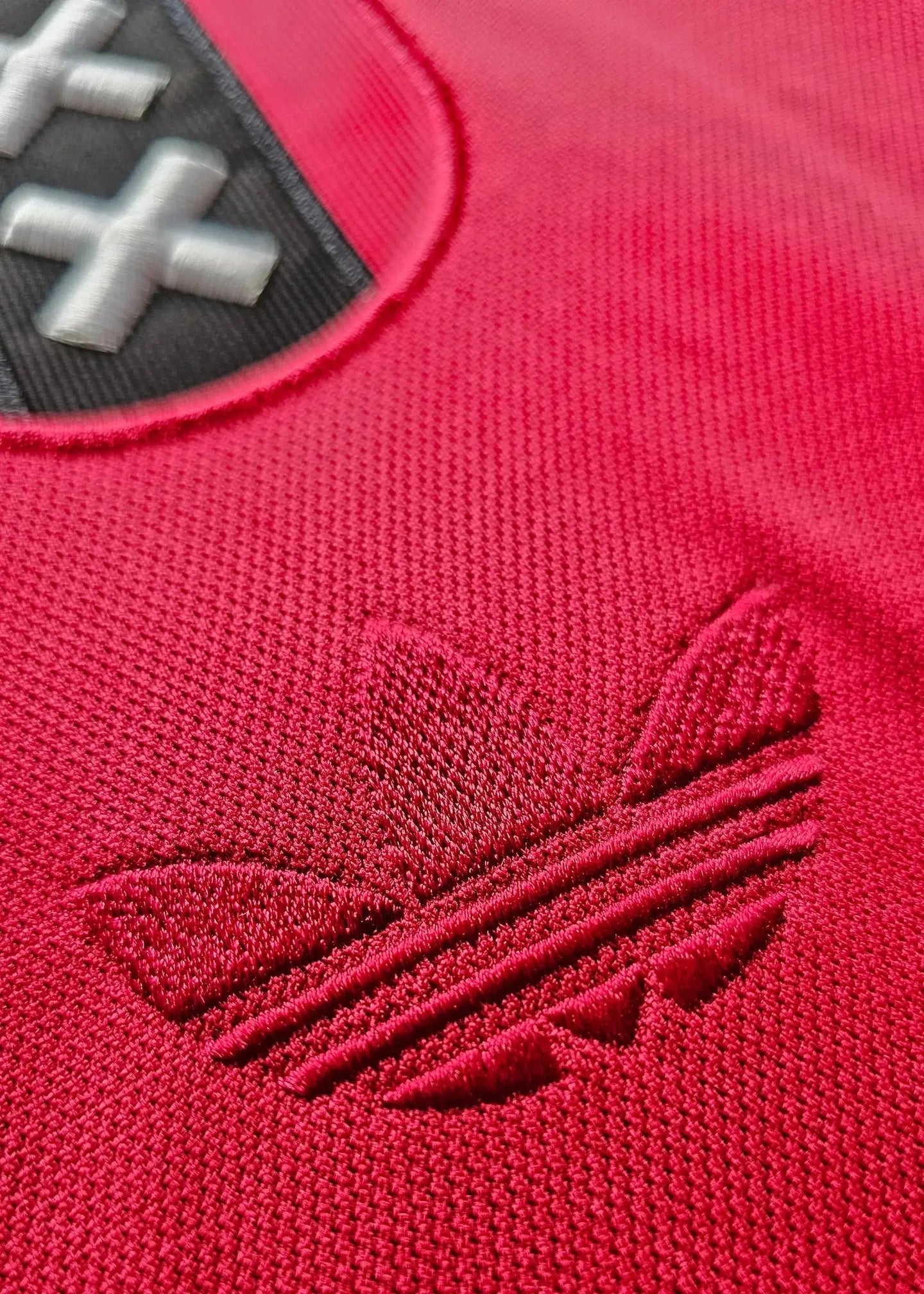 Detail of AFC Ajax crest in black and red with three stripes logo on a red fabric background.