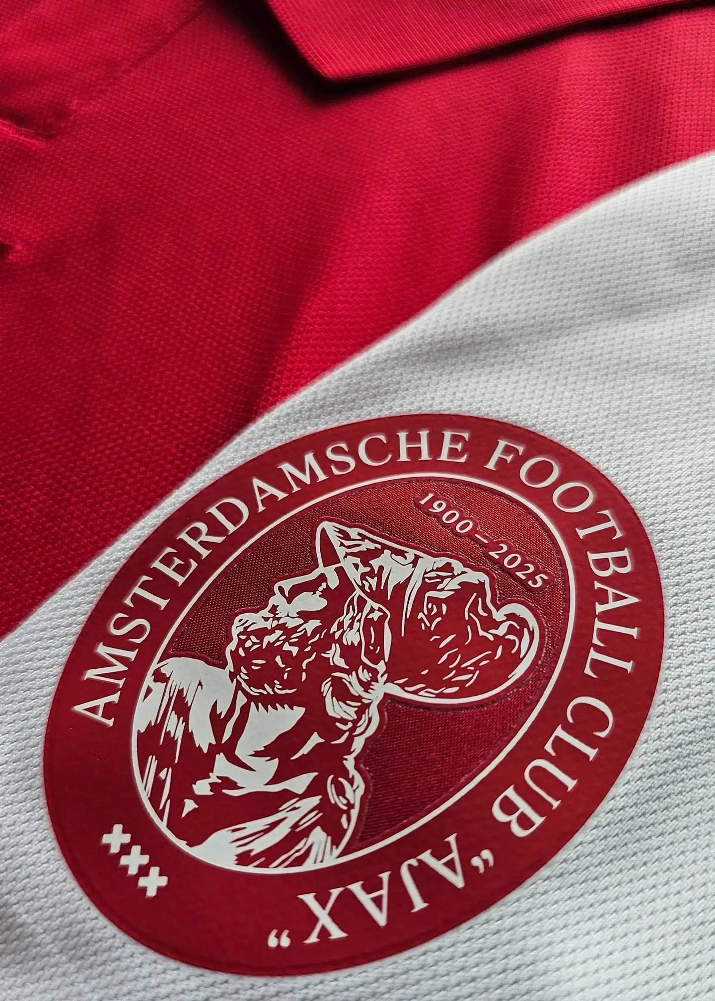 Crest detail of AFC Ajax featuring the text AMSTERDAMSCHE FOOTBALL CLUB and dates 1900-2025.