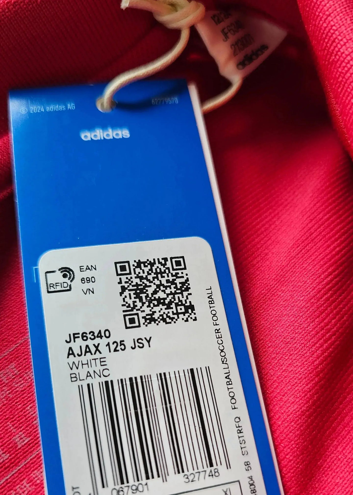 Tag showing Ajax 125 JSY, size and care details, with red fabric in background.