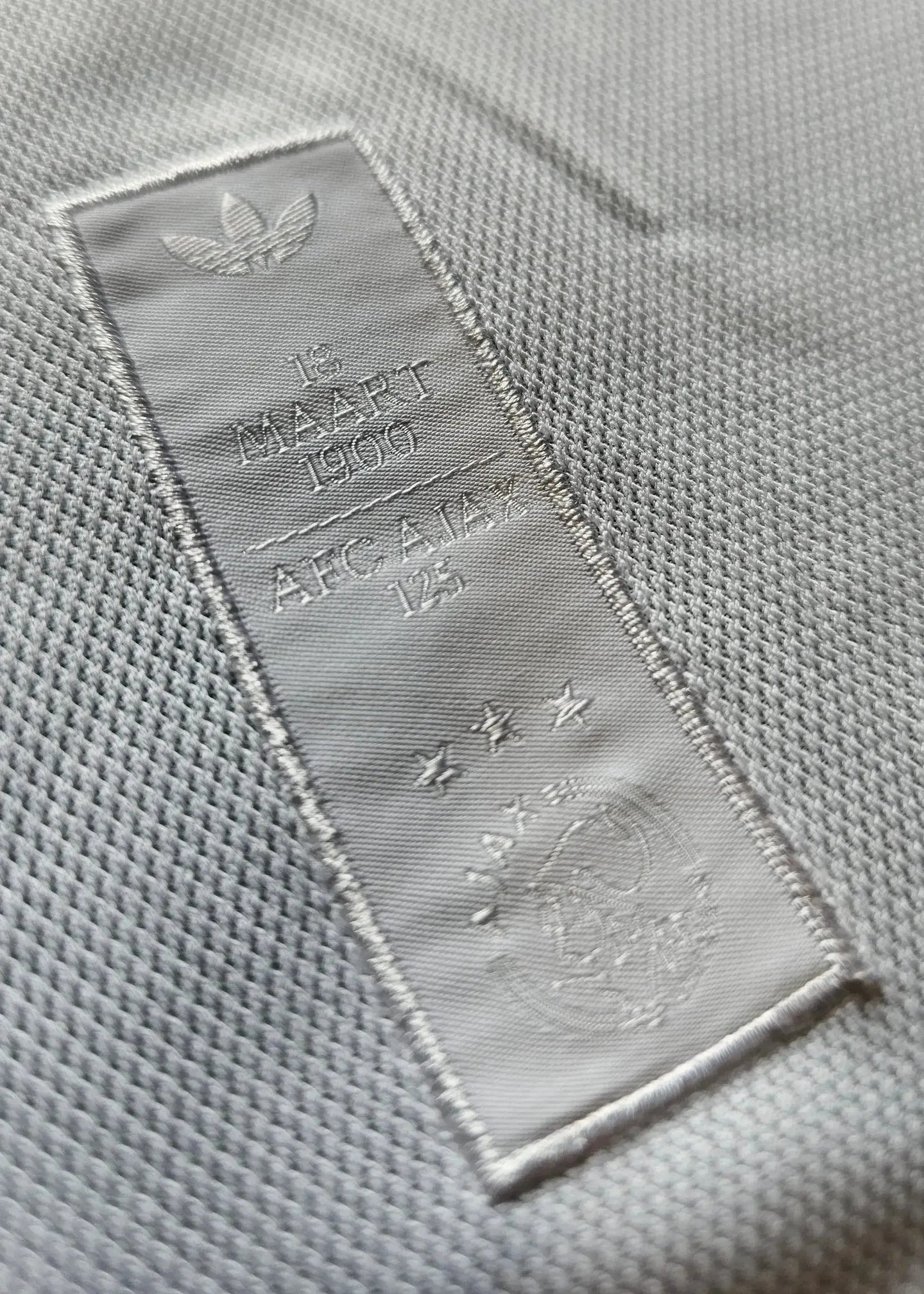 Detail view showing AFC Ajax 125th Anniversary tag with date 15 MAART 1900 and three stars.