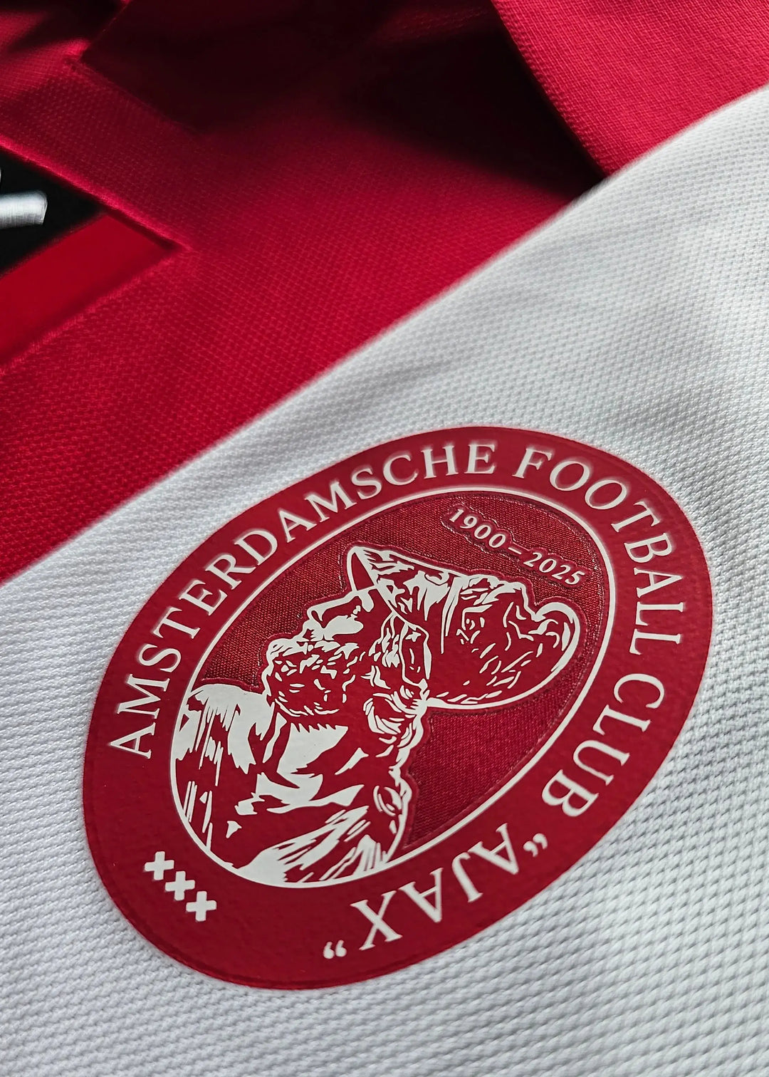 Detail showing the Ajax crest with the text 'AMSTERDAMS CHE FOOTBALL CLUB' and '1900-2025'.