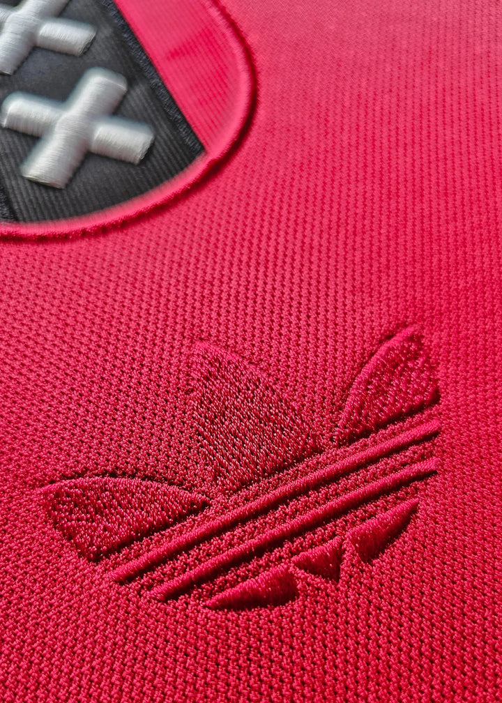 Close-up of the embroidered adidas logo on a red Ajax shirt.