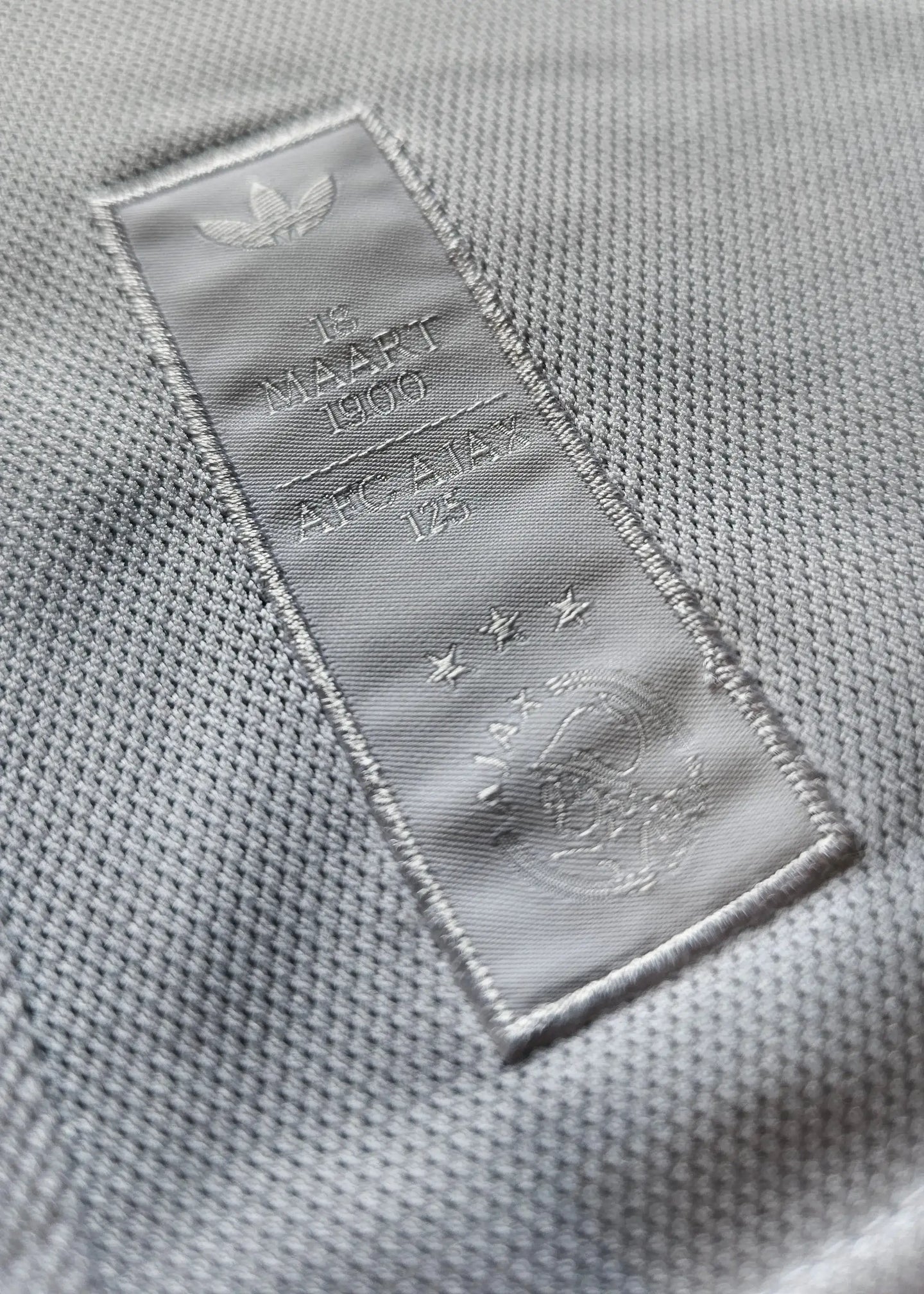Detail showing AFC Ajax 125th Anniversary patch with three stars and embossed '18 MAART 1900'.