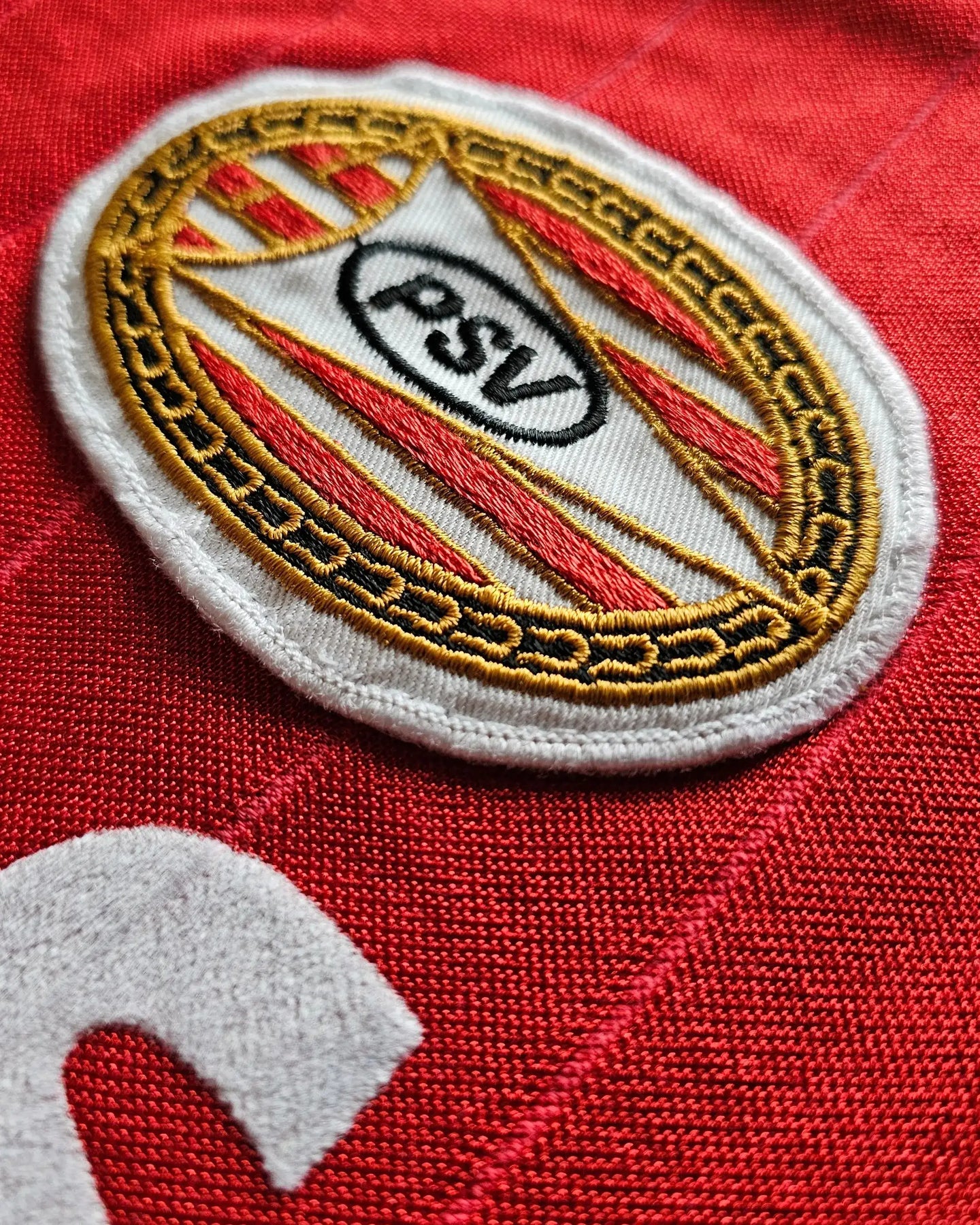 Close-up of the PSV Eindhoven crest on a red football shirt with intricate embroidery.