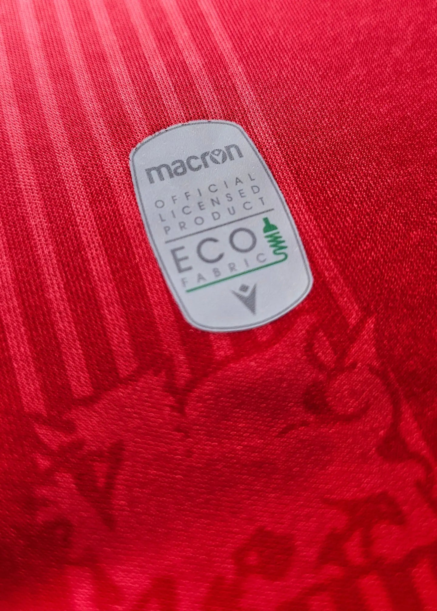 Crest detail featuring macron logo and ECO fabric label on red background.