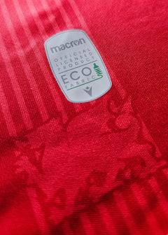 Detail view showing the eco-friendly fabric tag on a red Wrexham AFC soccer jersey.